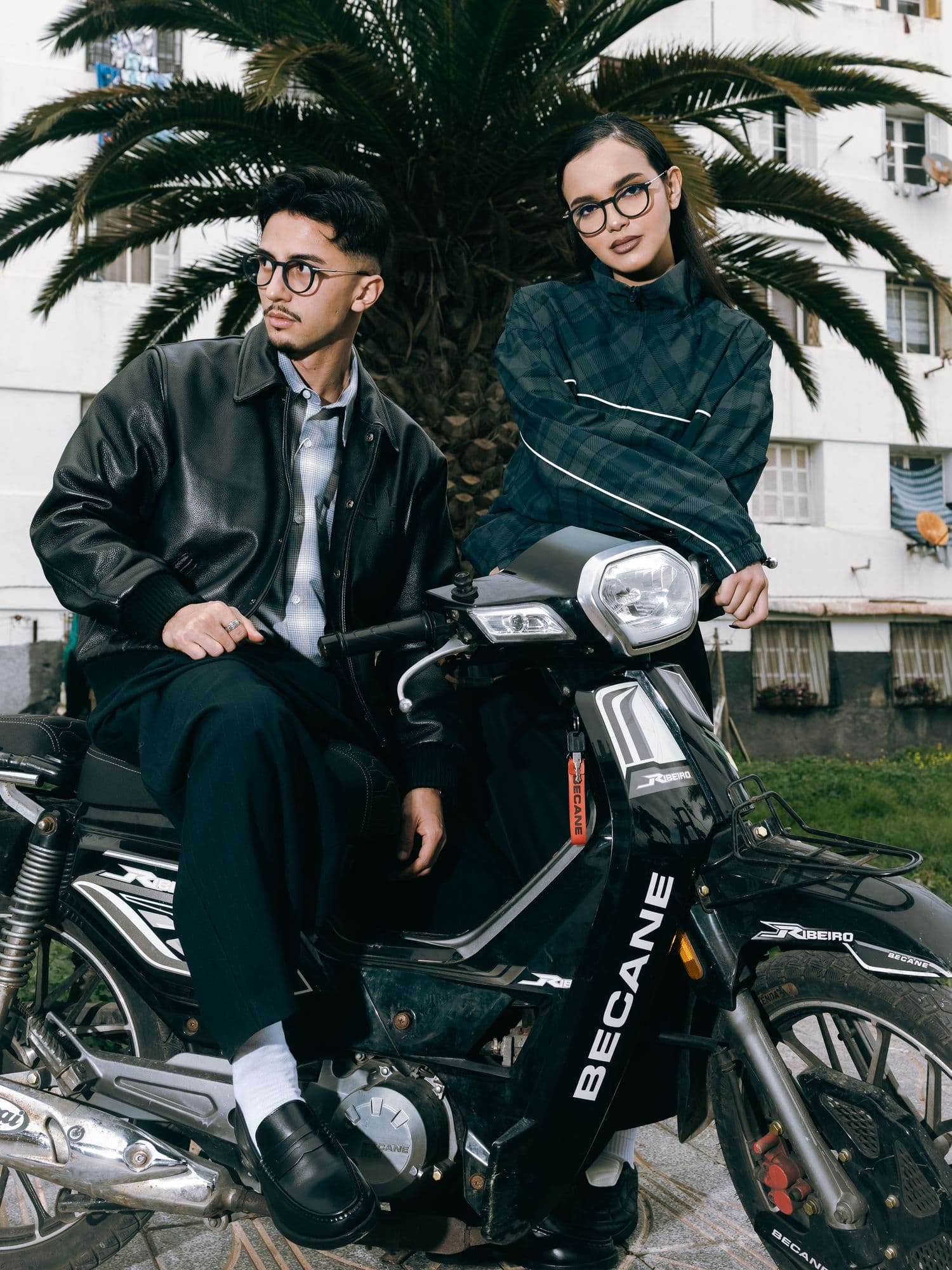 Two models on a scooter in front of a palm tree